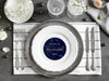 A nice wedding table setting is shown with a coaster in the center. Coaster features Love Never Fails design. This design has a dark blue marble background and the happy couples first name initials and wedding date in white writing.