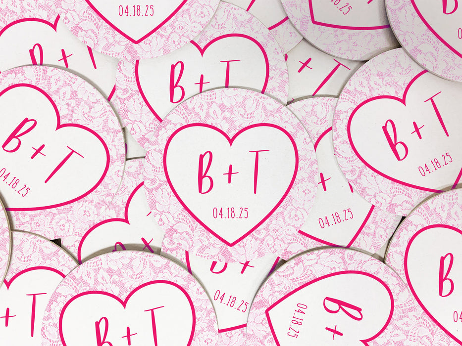 Coasters shown scattered on the surface of a table. Coasters feature Heart and Lace design. These are designed with the bride and groom first name initials and wedding date surrounded by a hot pink heart outline and light pink lace.