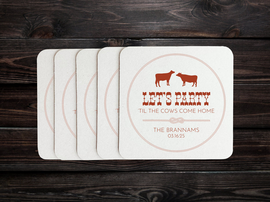 A stack of coasters are spread out across a dark wood surface. Coasters feature Til The Cows Come Home design. Design shows two cows with the saying Lets Party Til The Cows Come Home with newlyweds last name and wedding date.