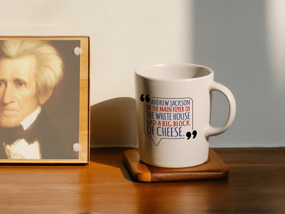 white mug on wooden coaster on wooden counter next to wooden frame with a picture of Andrew Jackson with an American west wing design and Typography that says Andrew Jackson in the Main Foyer of The White House had a Big Block of Cheese.