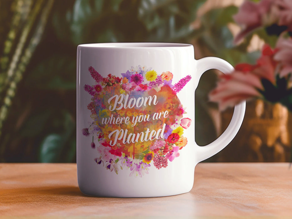 white mug on brown table surrounded by house plants and flowers with a floral design that says Bloom Where You Are Planted