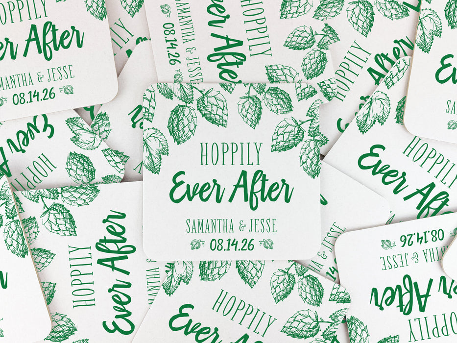 Square paper coasters are spread out across a table. Coasters feature Hoppily Ever After design. This design uses green lettering and sketched drawings of beer hops. Wedding couples names and date can be customized.