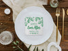 A nice wedding table setting is shown with a coaster in the center. Coaster features Hoppily Ever After design. This design uses green lettering and sketched drawings of beer hops. Wedding couples names and date can be customized.