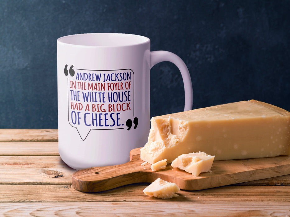 white mug with an American west wing design and Typography that says Andrew Jackson in the Main Foyer of The White House had a Big Block of Cheese. on a wooden table next to a block of cheese with a dark blue background