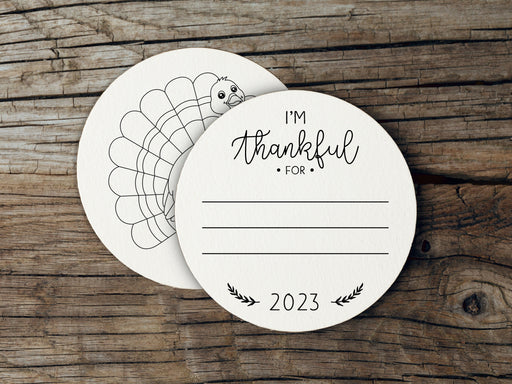 Front and back of coasters shown on a wooden background. Front of coasters show the text I'm thankful for, has lines for writing in a response, and current year. Back of coasters feature a turkey illustration.