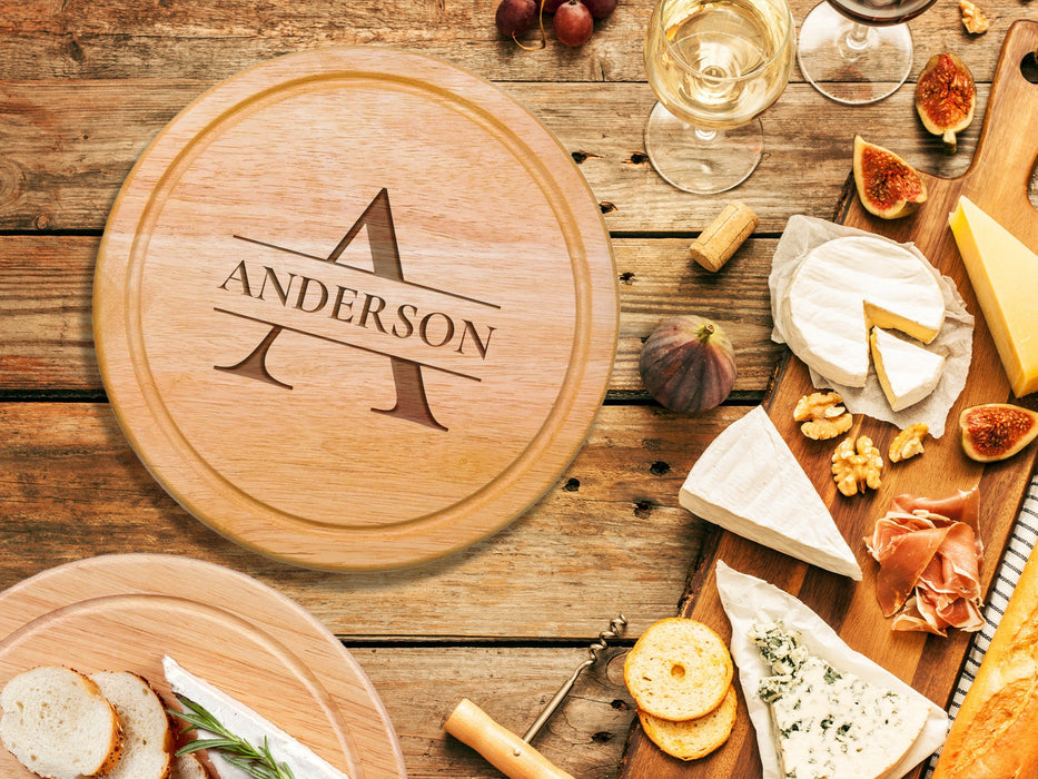 wooden cheeseboard on wooden table surrounded by wine glasses, figs, cheese, bread, crackers, Italian meats, and another charcuterie board engraving includes the name Anderson with the letter A