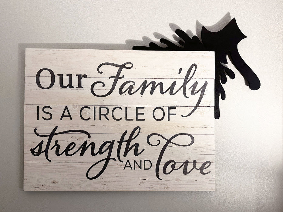 A black door frame topper, designed with the silhouette of an axe and blood splashes, is seen on top of wall art that reads, Our family is a circle of strength and love. The wall behind is grey blue.
