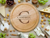 wooden cheese board surrounded by various cheeses, grapes, cheese knife tools, corn nuts, olives and walnuts  engraving is of the last name Campbell with the letter C