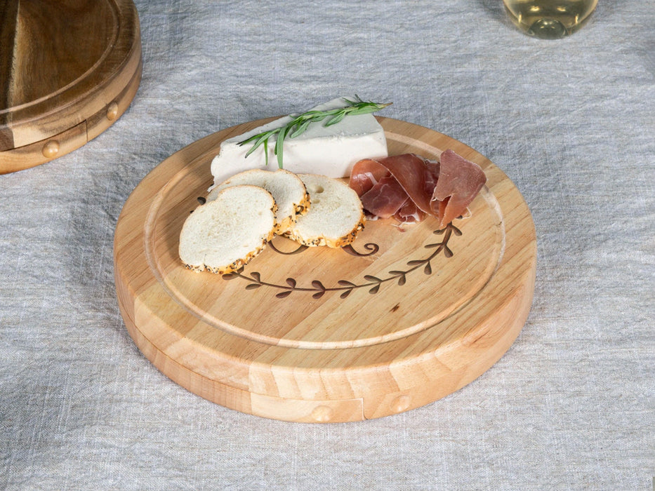 engraved cheeseboard on tabletop next to another cheeseboard with meats, cheeses, and bread ontop