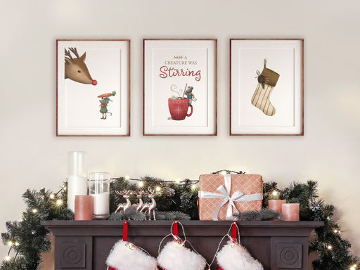 three christmas mice and stocking prints in wooden frames on white wall hanging above a fireplace surrounded by christmas decor such as pine leaves, candles, gifts, reindeer statues, stockings, and christmas lights