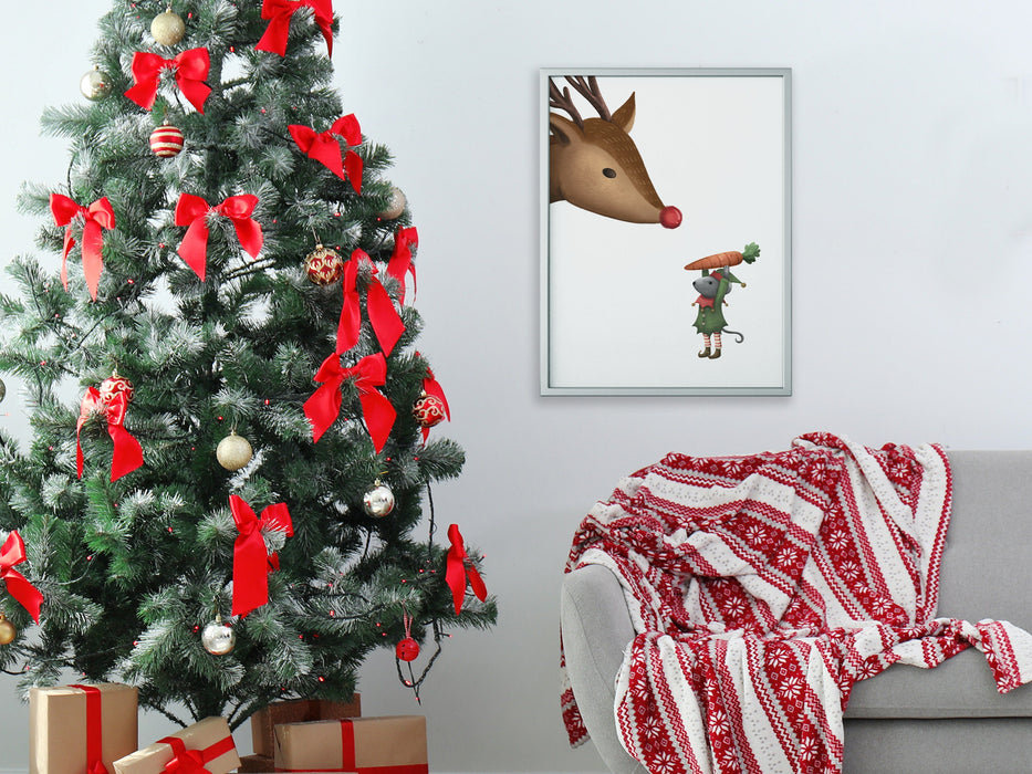 silver frame hanging on white wall with a christmas print of an elf mouse offering a carrot to a reindeer surrounded by holiday decor such as a christmas tree with bows and ornaments, christmas gifts, and a grey couch with a red and white blanket