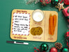 wooden Santa cookies and milk tray with a glass of milk, cookies, and carrots on top of a green background next to a dry erase marker surrounded by holiday decor such as pine leaves, holly berries, and christmas ornaments
