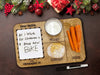 oak Santa cookies and milk tray with a glass of milk, cookies, and carrots ontop of a brown background next to a dry erase marker surrounded by holiday decor such as pine leaves, holly berries, and christmas ornaments