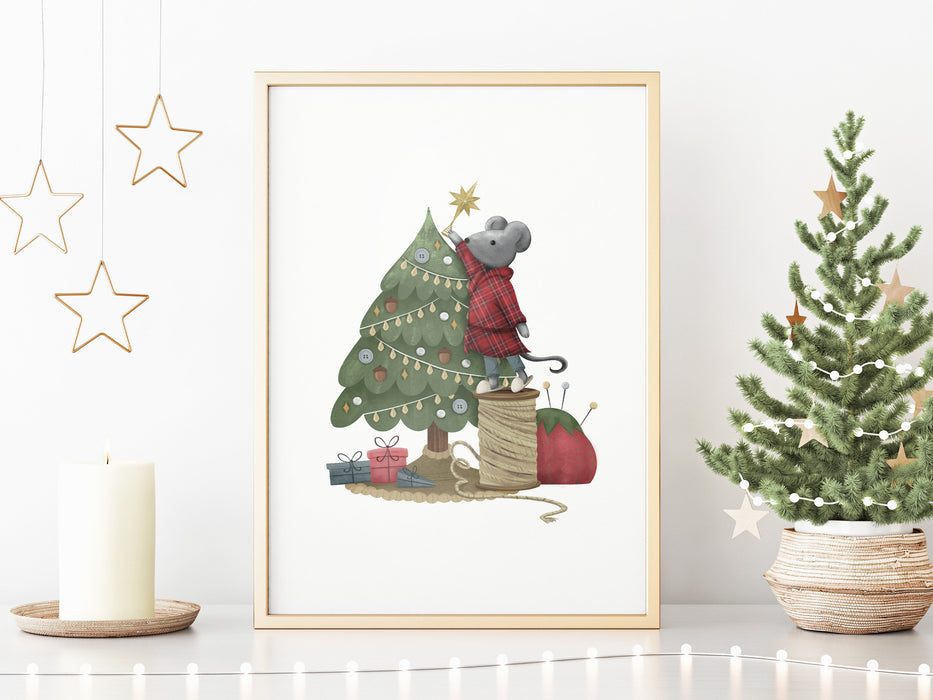gold framed Christmas print with mouse decorating tree surrounded by gold holiday decor such as a candle, gold stars, and a mini tree decorated with stars and mini lights