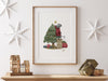 wooden frame hanging over wooden counter with christmas print of a mouse decorating a christmas tree surrounded by holiday decor such as white stars, mini wooden houses, and wrapped gifts