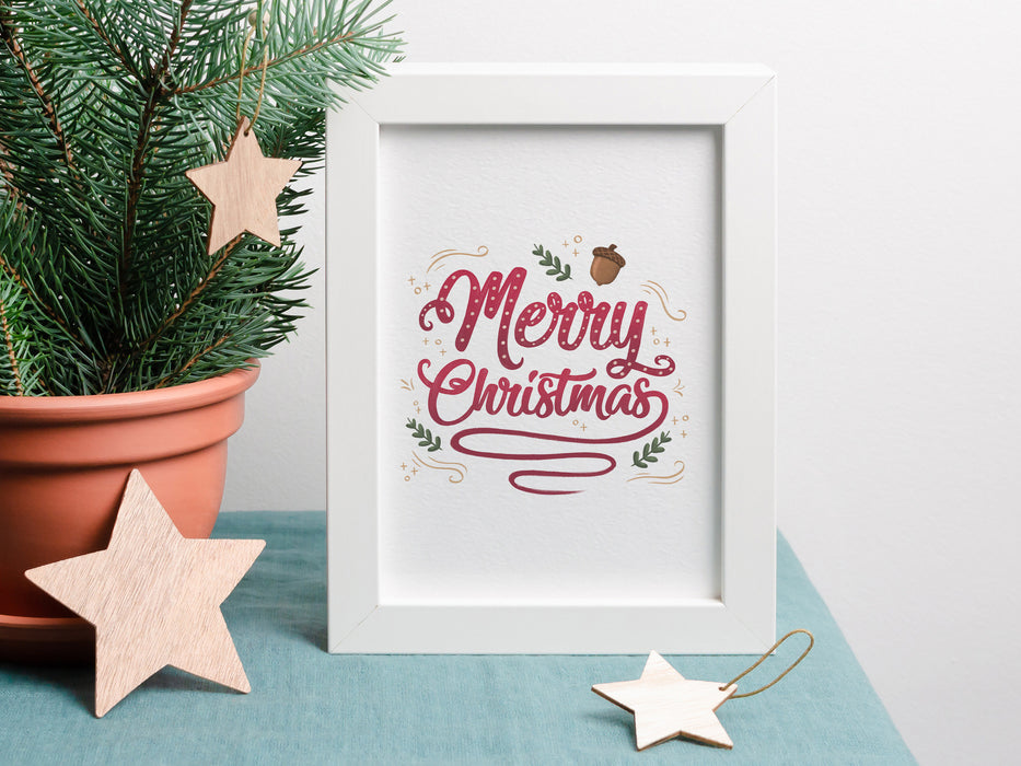 small merry christmas typography print inside a white frame ontop of a blue table cloth next to a mini pine tree surrounded by wooden stars