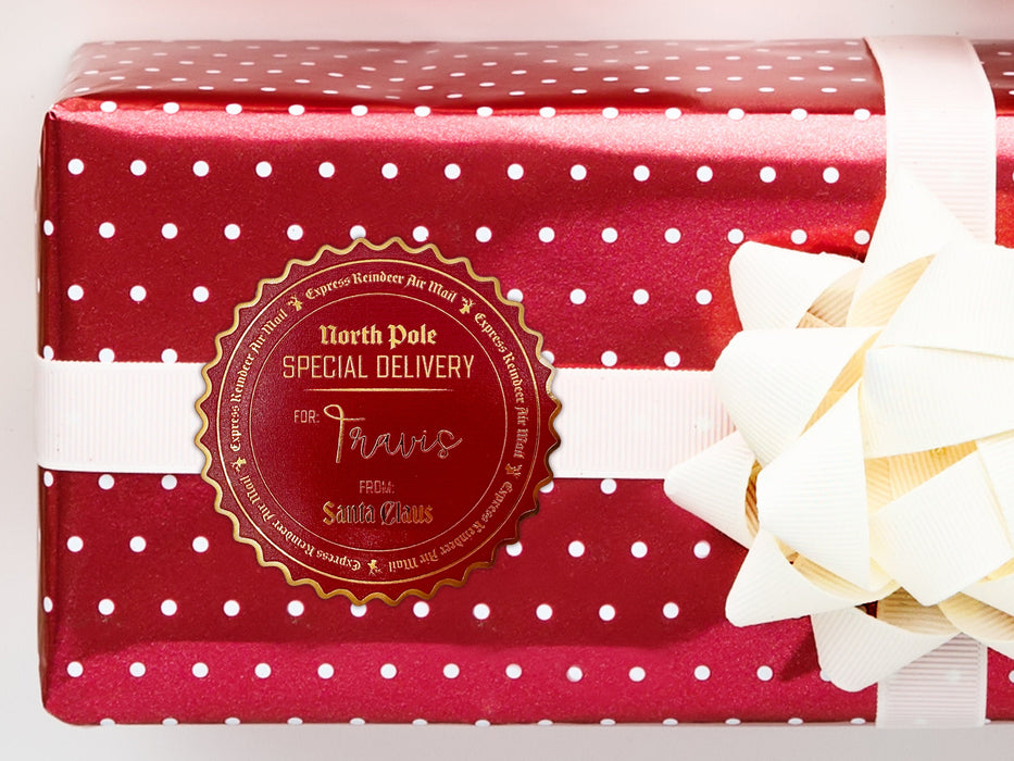 A gold foil cardstock Santa gift tag is shown on a Christmas present. The present paper is red with white polka dots. A white bow and ribbon are around the present. The box is seen on a white surface.