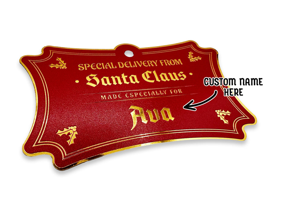 A hanging gold foil cardstock Santa gift tag is shown on a white surface. The text beside it reads, Custom Name Here.