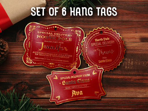 Text reads, Set of 6 Hang Tags. Three gold foil cardstock hanging Santa gift tags are shown on a dark wooden surface. Pine tree branches, a pine cone, a red ornament, and a Christmas present are shown around the tags.