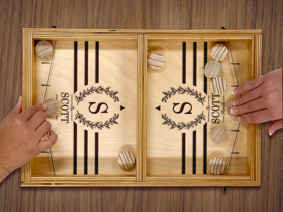 puck sling board game with an S monogram with wreath design that reads The Scott Family on wooden table with two hands playing with wooden puck discs