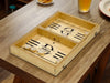 puck sling board game with an initial last name design that reads the letter D and says the name DeBaise with wooden discs on wooden table surrounded by plates of chips and a glass of juice