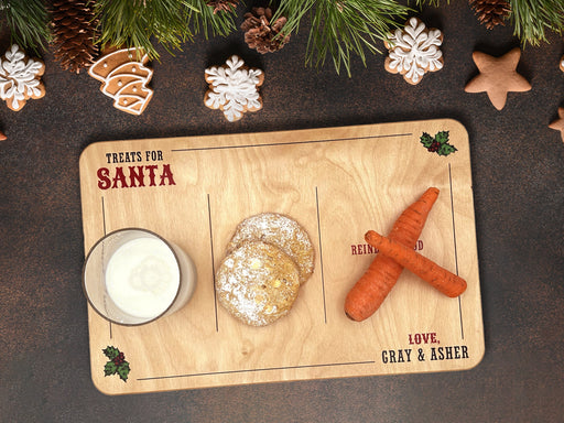 wooden treats for Santa wooden cookie tray that says Treats for Santa, Love Gray & Asher with a glass of milk, cookies, and carrots on it ontop of a brown table surrounded by cookies, pine cones, and pine leaves