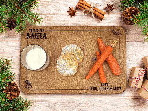 oak treats for Santa wooden cookie tray that says Treats for Santa, Love Gray & Asher with a glass of milk, cookies, and carrots on it, sitting ontop of a wooden table surrounded by holiday decor and pine leaves, spices, presents, and pinecones