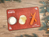 red treats for Santa wooden cookie tray that says Treats for Santa, Love Gray & Asher with a glass of milk, cookies, and carrots on it, sitting ontop of a wooden table surrounded by golden holiday decor and pine leaves