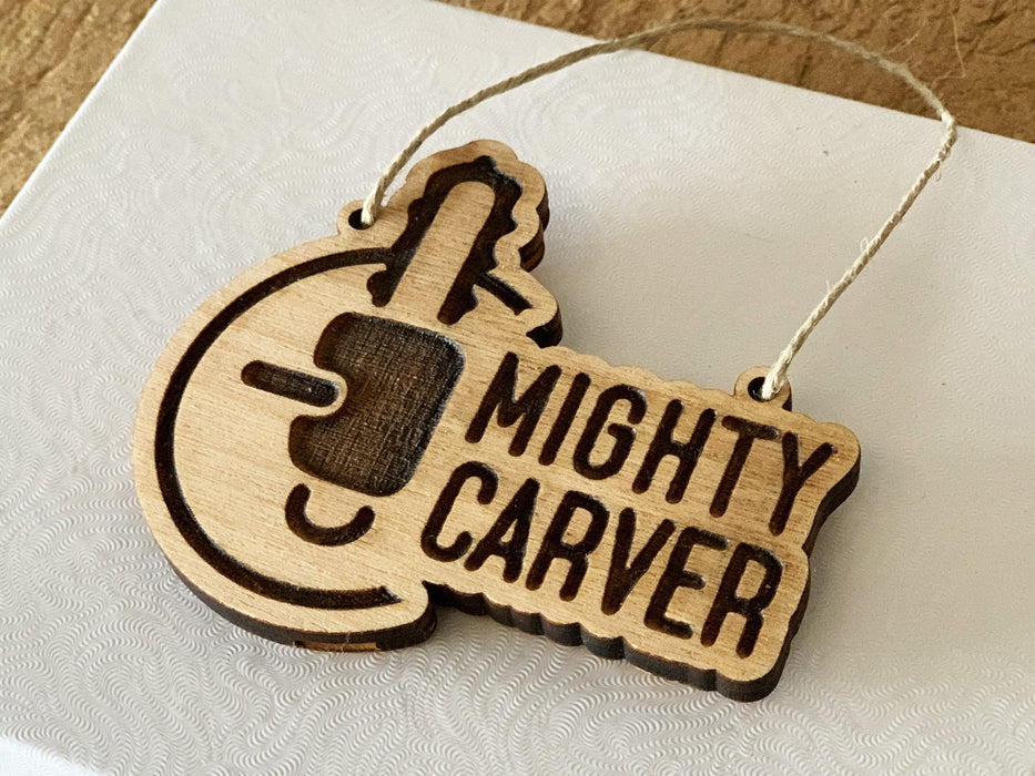 Custom ornament with Mighty Carver logo is shown against a white and wood background.