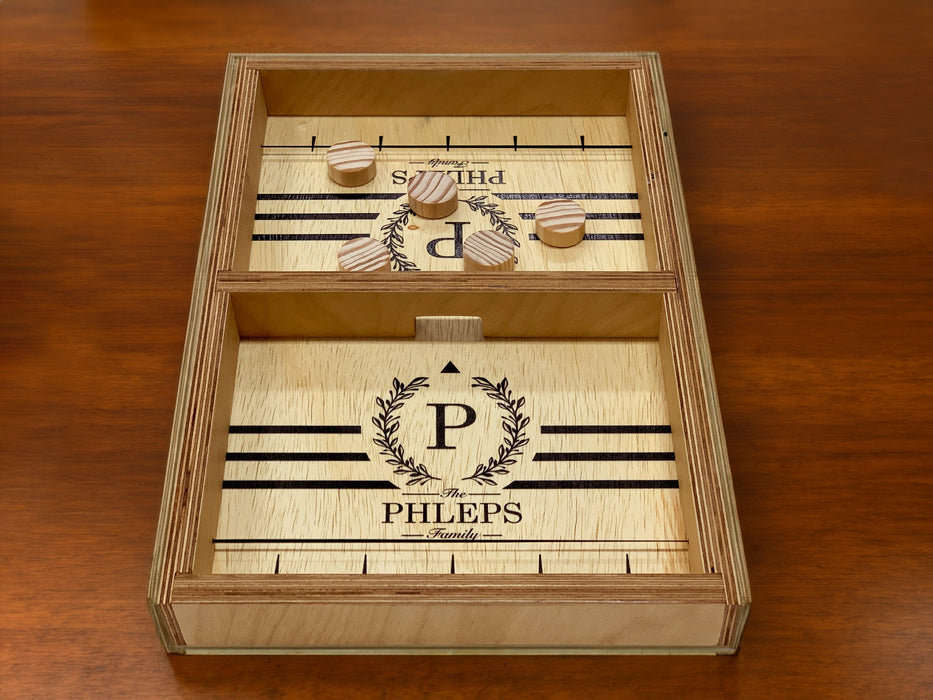 puck sling board game with an P monogram with wreath design that reads The Phleps Family with wooden puck discs on dark brown table