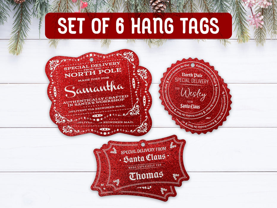 Text reads, Set of 6 Hang Tags. Six red glitter cardstock hanging Santa gift tags are shown on a white wooden surface. Pine tree branches, pine cones, and other foliage can be seen on the top of the image.