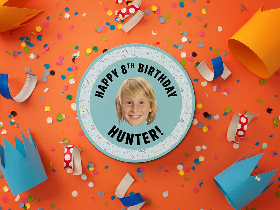 Coaster sits on an orange, decorated surface with birthday hats and confetti. Coaster is designed with multi-colored confetti, teal blues, and a custom face photo. Coaster text reads Happy 8th Birthday Hunter!