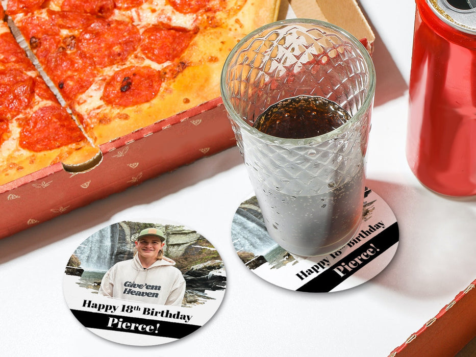 One coaster has a drink on it and an empty coaster sits beside it on a white table with pizza boxes. Coasters are designed with custom photo, text, and brushed elements. Coaster text reads Happy 18th Birthday Pierce!