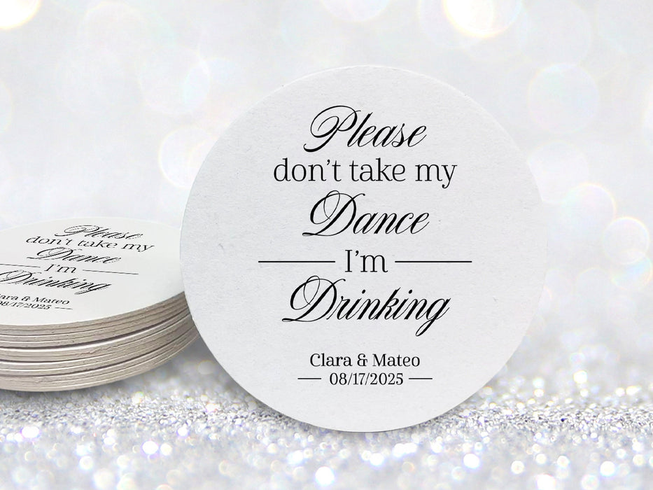 A single coasters beside a stack of coasters are shown against a silver glitter background. Coasters say Please don't take my dance, I'm drinking with wedding couple's names and wedding date on the bottom.