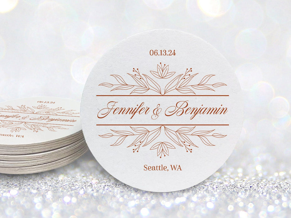 A stack of coasters by a single coaster in front of glittery background. Coasters feature a personalized floral design with the happy couple's first names, wedding date, and location.