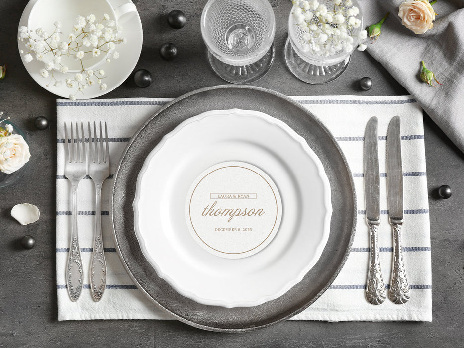A coaster is shown as a part of a place setting with flowers and silverware. Coaster features a personalized design with the happy couple's first names, last name, and wedding date.