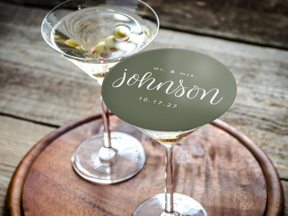 One coaster is shown being used as drink cover on top of a martini glass. Coasters feature a custom last name design with a married couple's last name and wedding date.
