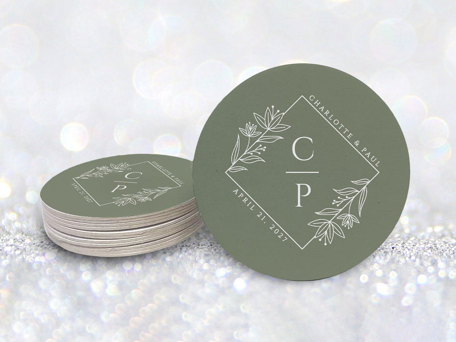A stack of coasters by a single coaster in front of glittery background. Coasters feature a floral diamond design with a monogram, wedding couple's names, and wedding date.