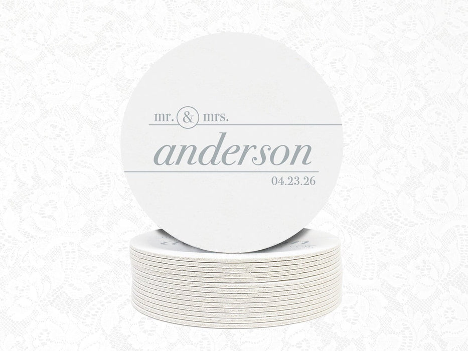 A stack of white round wedding coasters on top of each other. Coasters feature a custom design with a wedding couple's last name and wedding date.