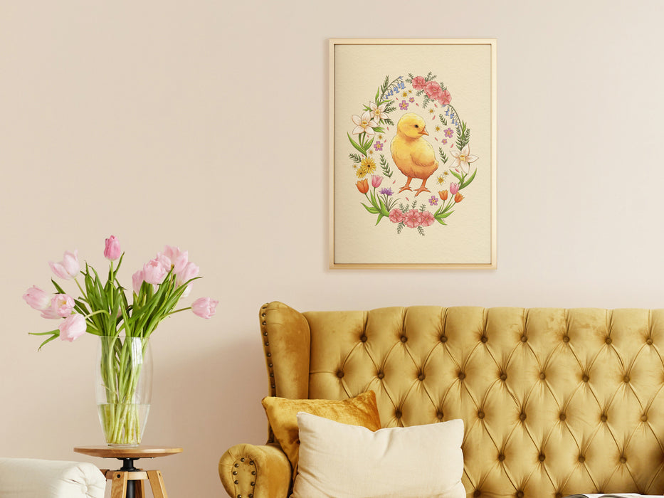easter print of a baby chick surrounded by spring flowers in a gold Frame on a white living room wall surrounded by decor and furniture such as a couch, pillows, a side table, and tulips in a vase