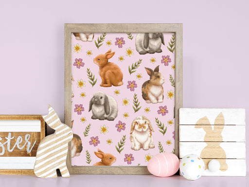 easter print of pastel bunny and flower pattern in a wooden frame on a wooden counter surrounded by easter decor such as bunny statues, signs, and decorated easter eggs in front of a purple background
