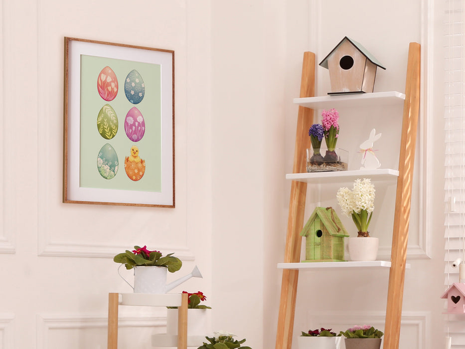 easter print of with pastel easter art print of decorated eggs with a baby chick in a wooden frame on white wall in living room surrounded by easter decor such as potted plants, flowers, and bird houses,