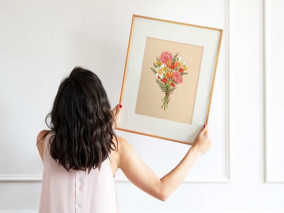woman with black hair and pink shirt holding up a wooden frame with a pastel easter print featuring a spring bouquet of colorful flowers
