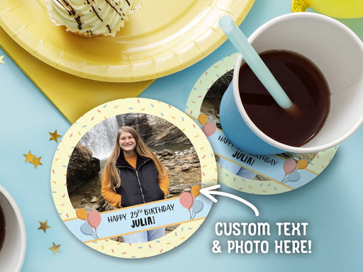 One coaster has a drink on it and an empty coaster sits beside it on a decorated table. Coasters are designed with multi-colored confetti, yellow, blue, and a custom photo. Coaster text reads Happy 25th birthday Julia!
