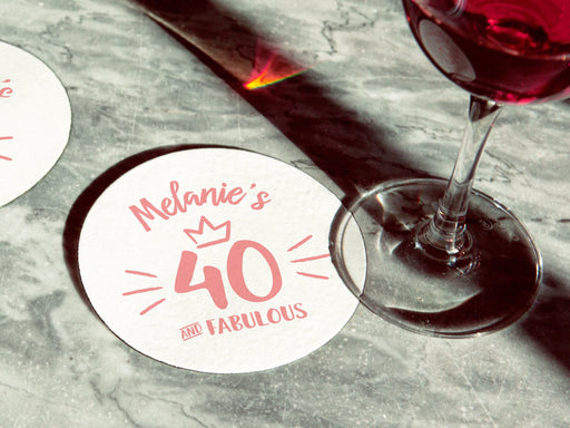 Two coasters are shown on a marble surface. One has a wine glass on it. Coasters are designed with pink ink. Coaster text reads Melanie's 40 and Fabulous.