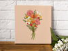 12x12 inch canvas with spring bouquet pastel easter art in front of a white brick wall with small white flowers in front of the canvas on a wooden table