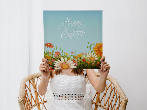 a woman in a white dress sitting in a wicker chair holding a 12x12 canvas of happy easter artwork of a spring meadow in a living room with white walls and curtains