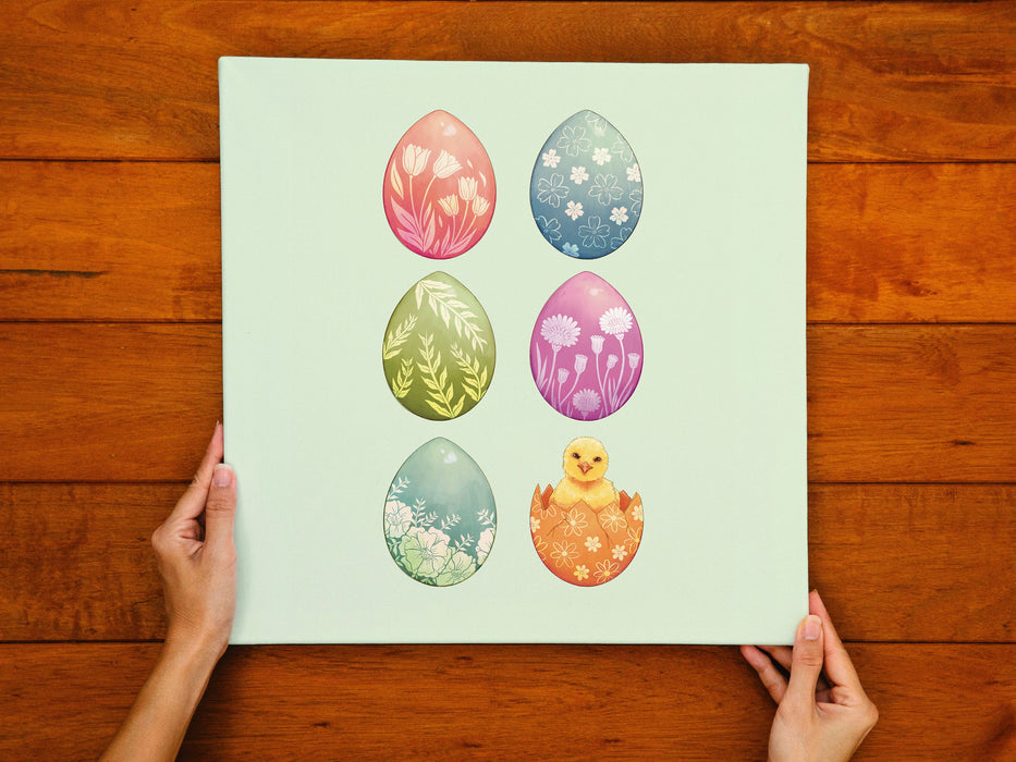 two hands holding a  12x12 canvas with colorful easter artwork of rows of eggs and a baby chick on a wooden table