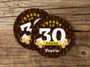 Two coasters are shown on a wooden surface. Coasters say Cheers to 30 Years, Travis!