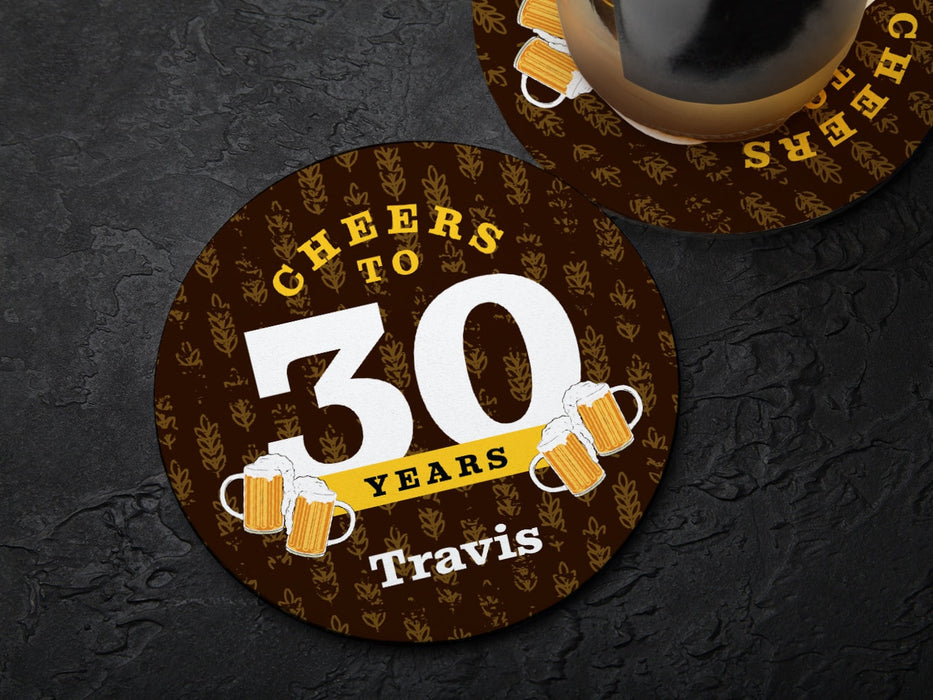 One coaster has a drink on it and an empty coaster sits beside it on a black background. Coasters say Cheers to 30 Years, Travis!